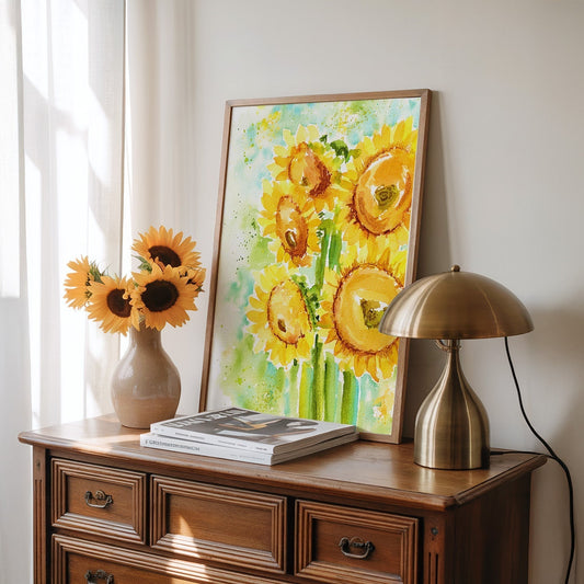 Framed sunflower painting on a dresser with flowers, books, and a lamp in soft light.